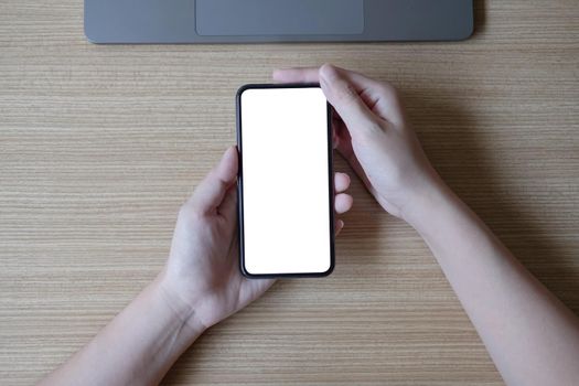 Woman hand holding smartphone with blank white screen on workplace.