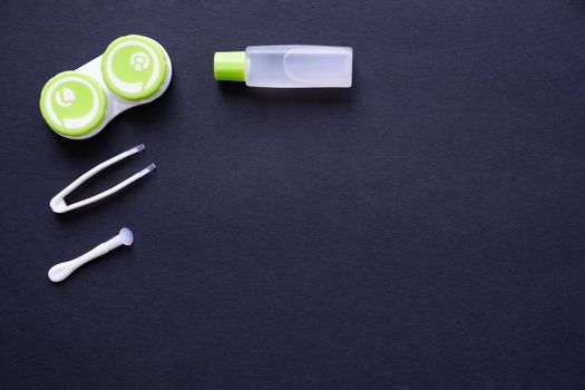 Container with contact lenses, tweezers, suction cup and bottle with solution on dark blue background, top view, copy space