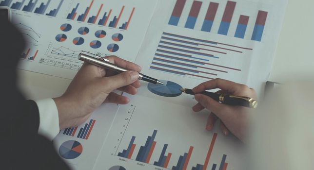 Close-up of two women's hands pointing to a turnover chart while talking on a wooden table in the office. group support concept