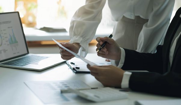 Close up team businesswoman studying statistics and holding a graph document by hand An office worker stood near the desk with a laptop. woman pointing finger