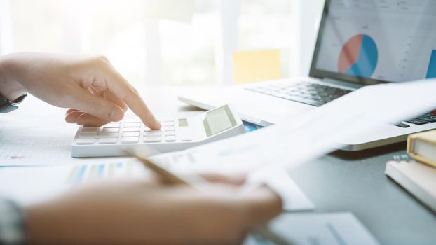 Close up Businessman and partner using calculator and laptop for calculating finance, tax, accounting, statistics and analytic research concept.