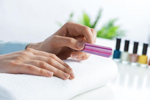 Woman using nail file and create perfect nails shape. Grinding female nails with nail file tool and preparing for apply nail polish. Woman doing herself nail care procedure at home. Beauty and hygiene