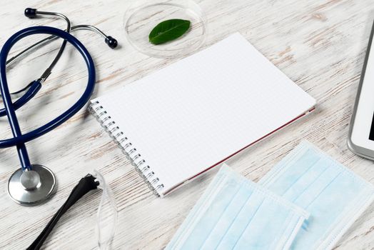 Patient examination and consultation concept with doctor workplace. Spiral notepad, disposable face mask, stethoscope and cardiogram on wooden surface. Professional healthcare in medical center.