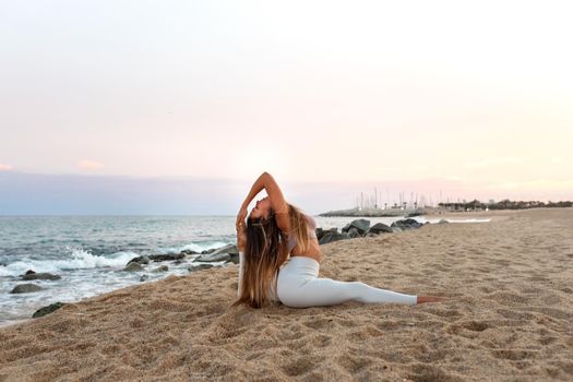 Flexible young caucasian woman practicing the splits yoga pose on the beach at sunset. Copy space. Spirituality and healthy lifestyle concept.