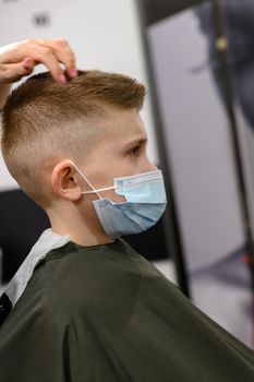 Schoolboy in a barbershop during a pandemic, stylish haircut for baby, hair styling with gel and hair dryer.