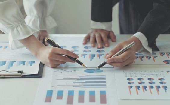 Close-up of two women's hands pointing to a turnover chart while talking on a wooden table in the office. group support concept