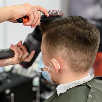 Teen guy gets a haircut during a pandemic in a barbershop, haircut and drying hair after a haircut, styling hair after a haircut with a hair dryer.