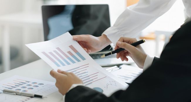 Close up team businesswoman studying statistics and holding a graph document by hand An office worker stood near the desk with a laptop. woman pointing finger.