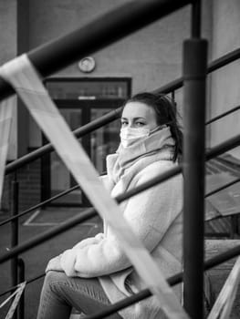 Photo of a girl in a mask. Sitting on the street with danger warning tapes. isolated Covid-19 pandemic.