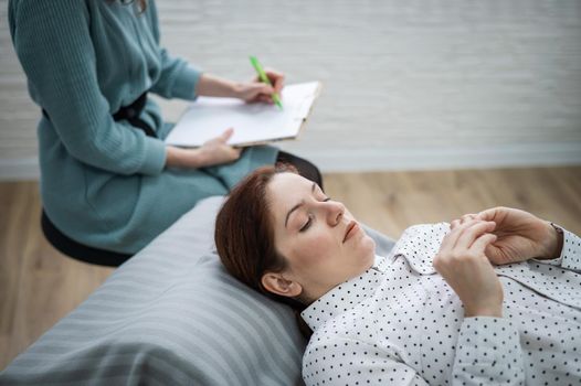 A caucasian woman lies on a couch and expresses her feelings, while a psychologist makes notes on a tablet