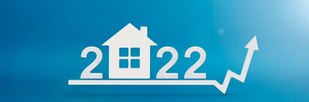 Real estate value in 2022. Rising costs of construction, insurance, rent and mortgages. inflation and rising prices. Model of a house on a blue background. Numbers 2022 on up arrow.