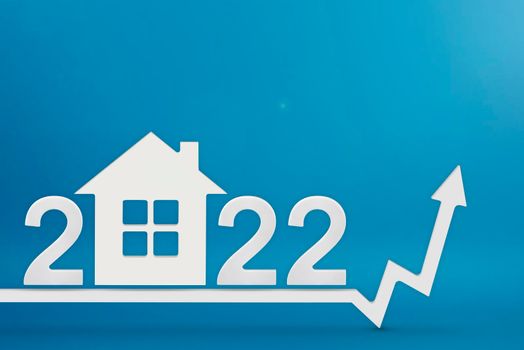 Real estate value in 2022. Rising costs of construction, insurance, rent and mortgages. inflation and rising prices. Model of a house on a blue background. Numbers 2022 on up arrow.