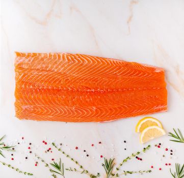Food background, large salmon fillet and seasonings on white cream marble table, flat lay, copy space.