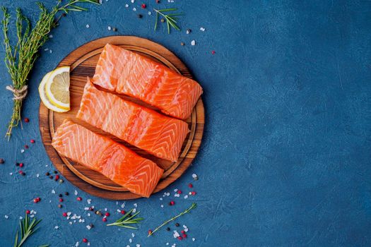 Food background, sliced portions large salmon fillet steaks on chopping board on dark blue concrete table, copy space, top view.