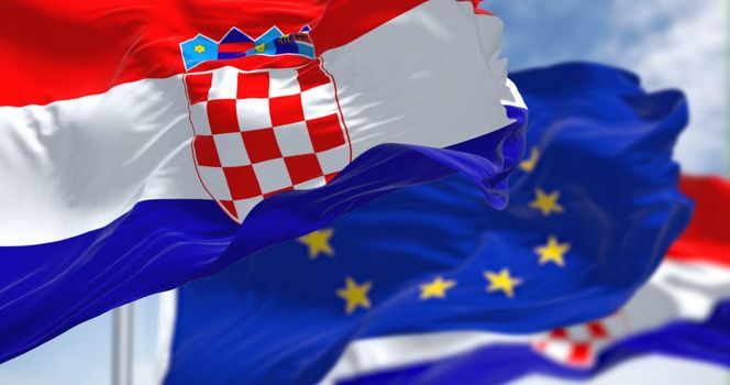 Detail of the national flag of Croatia waving in the wind with blurred european union flag in the background on a clear day. Democracy and politics. European country. Selective focus.