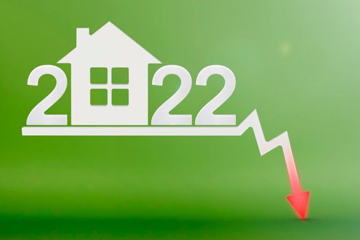 Real estate value in 2022. Sale and collapse of the value of real estate. inflation and rising prices. House model on a green background. Numbers 2022 on the down arrow.