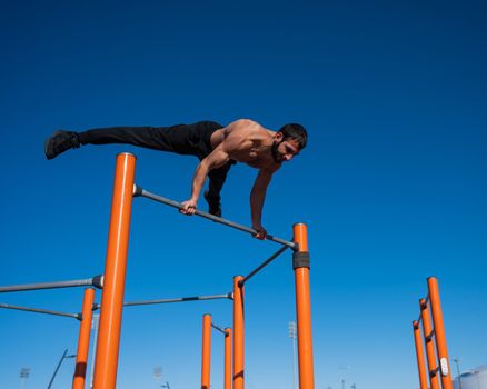 A man with a naked torso makes a balance on the horizontal bar