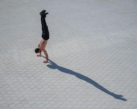 Shirtless man walks on his hands outdoors. View from above