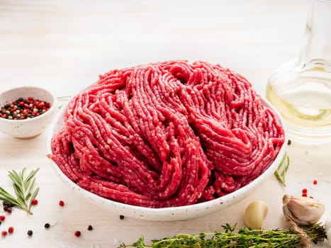 Mince beef, ground meat with ingredients for cooking on white wooden rustic table, side view, close up