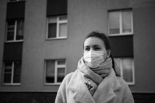 Shot of a girl in wearing face mask for protection, on the street. Against the background of a residential building with windows. lockdown Covid-19 pandemic.