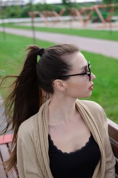 portrait of brunette woman with ponyrail sitting on a bench in park. nature lovers, attractive girl