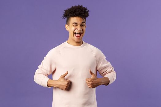 Portrait of enthusiastic lively, attractive young guy winking encourage join team, start career at this company, show thumbs-up with recommendation, give good advice, like and approve.