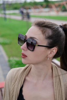 attractive brunette woman sitting on a bench in park. fashion clothes, stylish look.