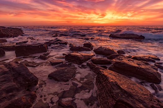 Rocks on the stone beach at sunset. Twilight sea and sky. Dramatic sky and clouds. Nature landscape.