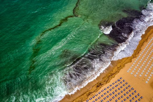 Aerial view of an amazing beach with white umbrellas, lounge chair, and turquoise sea. Tropical sea beach coastline, summer holiday.