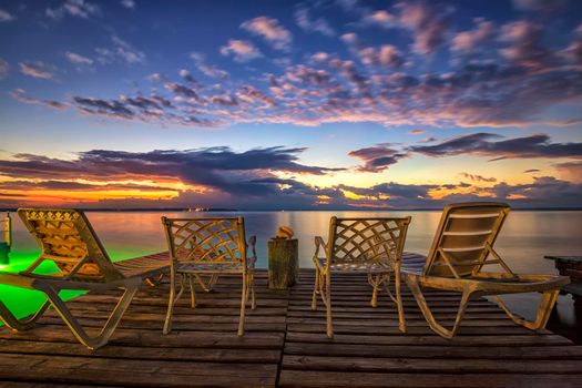 Empty deck chairs and chairs on a wooden pier waiting for sunrise on the sea beach.