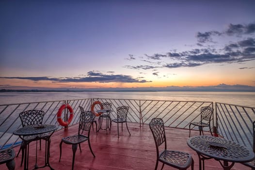 A couple of empty chairs and tables at sunrise on the sea beach.