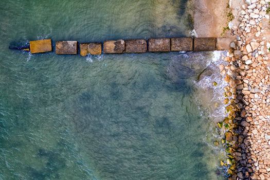Aerial top view from drone to the seacoast and old concrete pier, summer sea background.