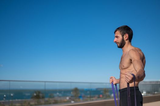 Shirtless man doing exercise with rubber bands outdoors