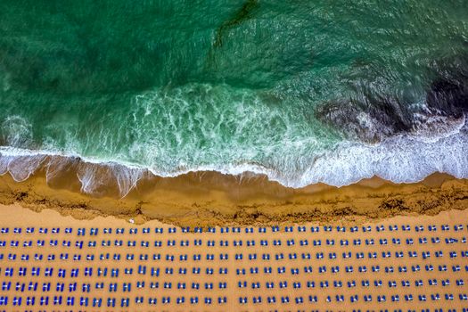 Aerial view of an amazing beach with white umbrellas, lounge chair, and turquoise sea. Tropical sea beach coastline, summer holiday.