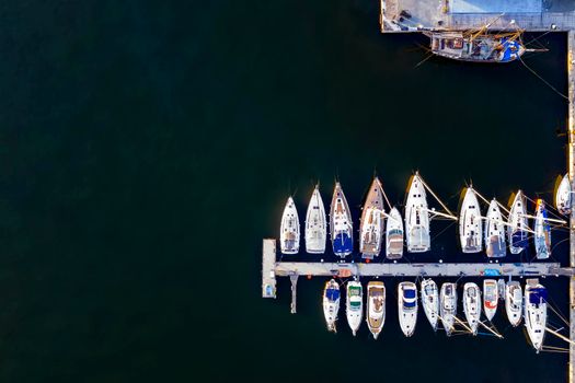 Aerial View by Drone of yachts and small motor boats. White boats in sea water. Yacht and sailboat are moored at the quay. Parking