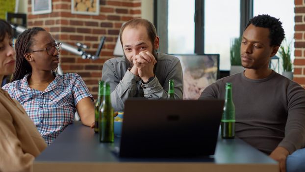 Men and women watching live videos on social media website, using laptop technology to see TV show together in living room. Modern people having fun with online wireless network.