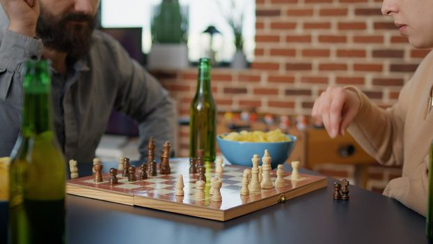 Cheerful people having fun with chess play at board games gathering together, drinking beer and eating snacks. Group of friends enjoying intelligence match for entertainment at home.