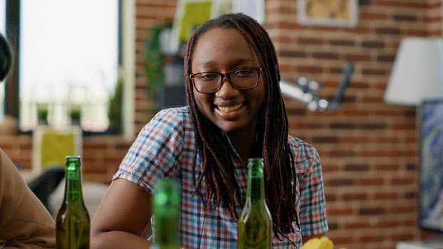 Portrait of happy woman looking at people playing chess game, having fun with board games and beer. Young adult enjoying meeting with friends for leisure activity with competition.
