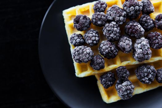 Belgian wafers with frozen blackberries on a black background.