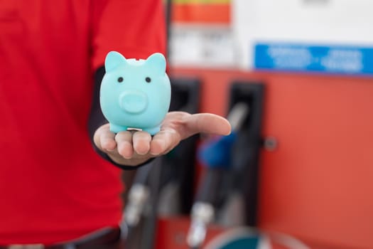 Gas station staff worker with piggy bank for save money from low fuel price, gas costs reduction, cut and saving gasoline drop price concept.