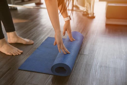 Healthy woman rolling preparing yoga mat for fitness class