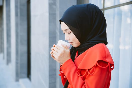 Arab Muslim women drinking coffee in the morning outdoor, Asian businesswoman young girl smiling hand hold coffee cup standing closeup.