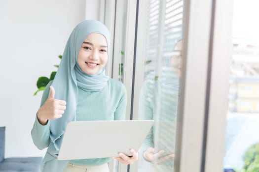 Asian Muslim Islamic woman with hijab happy enjoy working in office with laptop computer.