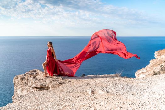 A girl with loose hair in a red dress stands on a rock rock above the sea. In the background, the sea and the rocks. The concept of travel.