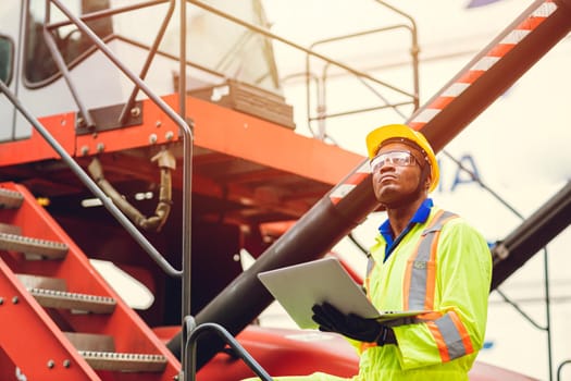 Black African port shipping staff director working in logistic using laptop to control loading containers at ship cargo for import export goods foreman looking high for future.