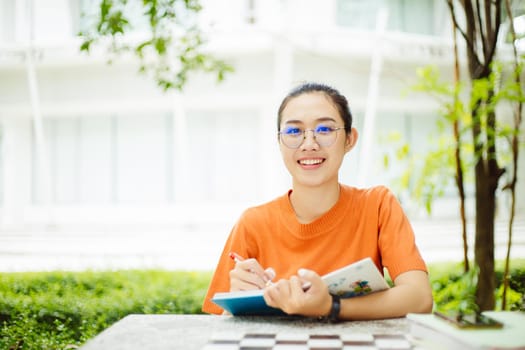 Portrait of nerd Asian woman girl smart teen happy smiling with glasses at green park outdoor in university campus with copyspace