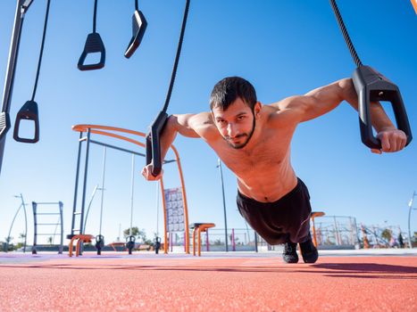 Shirtless man doing loop exercises outdoors