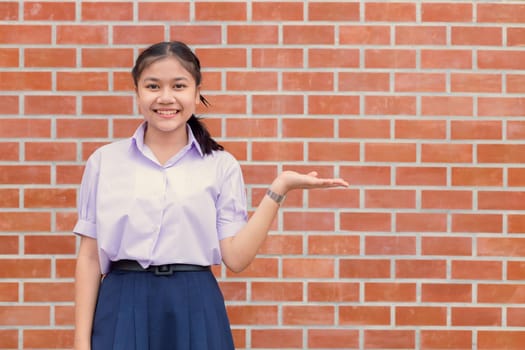 Asian girl teen student uniform happy smile with hand presentor showing display wall copy space.