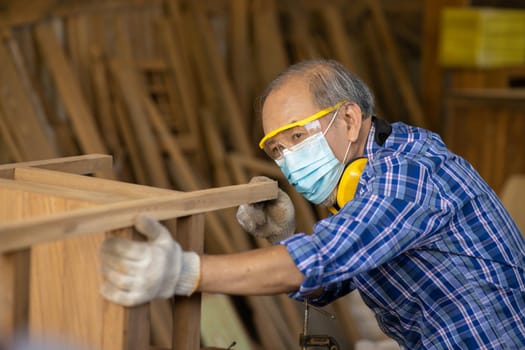 Elder worker wood woodcraft retire hobby for good retirement, Asian male mature professional master of making wooden furniture with face mask protective.