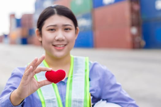 Girl teen worker in cargo container shipping port working with heart and good service mind concept. selective focus at red heart.